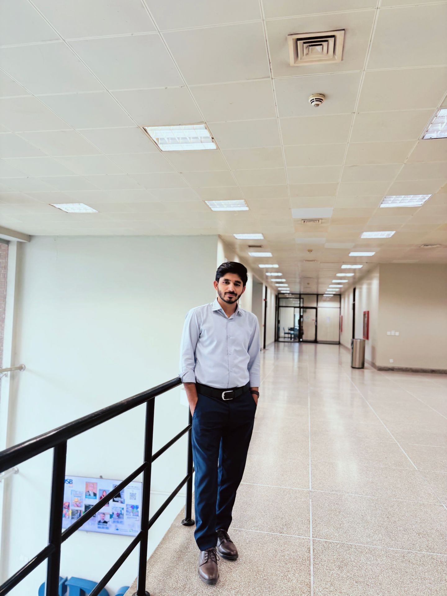 Man in business attire standing in a spacious hallway with bright overhead lighting and tiled floors.